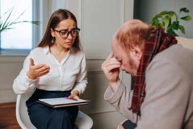 Gözlüklü bir kadın, sorunlu bir yüz ifadesine sahip bir erkek gibi dikkatle dinler ve doğal ışık dolu rahat bir ofiste danışmanlık sırasında duygularını ifade eder..