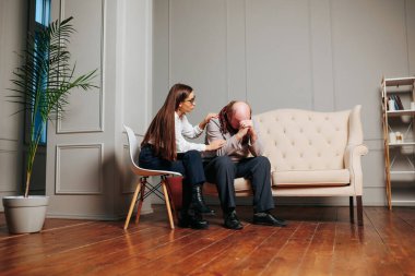 Bir kadın, sıkıntılı bir adamı rahat bir oturma odasında teselli eder. Sıcak atmosfer, destek ve anlayışın önemini vurgulayarak duygusal etkileşimlerini vurgular..