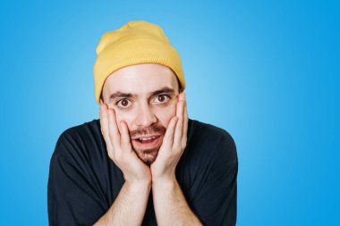 Sarı bereli bir adam şaşırmış görünüyor, yüzünü şaşırtıyor. Canlı mavi arkaplan, o anın neşeli ve neşeli havasını arttırır..