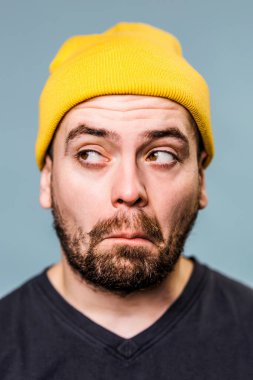 Parlak sarı bereli bir adamın yüzünde şakacı ve biraz şaşkın bir ifade vardır. Katı mavi arka plan onun küstah tavrını artırıyor ve kontrastlık ekliyor.