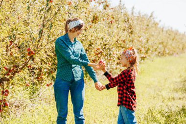 Bir kadın ve bir çocuk yemyeşil bir meyve bahçesinde neşeyle elma topluyor. Gülüşleri ve kahkahaları paylaşırken güneş ışıl ışıl parlıyor, çiçek açan elma ağaçlarıyla çevrili..