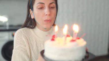 Doğum günü pastasındaki mumları tek başına söndüren bir kadın, evde sakin ve içsel bir kutlamayı simgeliyor..