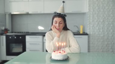 Evde sessiz bir doğum günü kutlaması, mutfakta yalnız başına oturan bir kadını yakar, yalnızlığı ve hayatı yansıtır..
