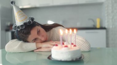 Yalnız bir kadın doğum gününü evde sessizce kutluyor. Pasta, mumlar ve düşünceli düşüncelerle. İyi aydınlatılmış mutfağında oturuyor..