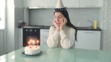 Düşünceli bir kadın mutfakta tek başına oturur, doğum gününü küçük bir pasta ve mumlarla kutlar, yalnızlık anındaki hayatı yansıtır..