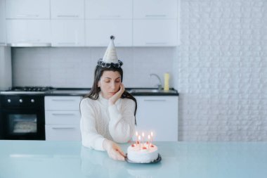 Bir kadın, elinde yanan bir pastayla masada oturmuş yalnızlığın ve kişisel anların özünü resmederken doğum gününü yansıtır..