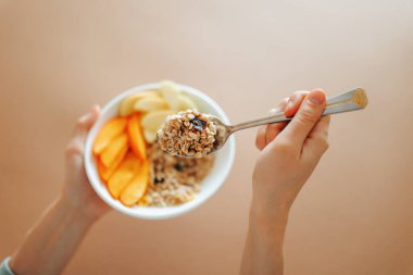 Bir insan içi yulaf dolu bir kaşığı taze meyvelerle dolu bir kaseden yemeye hazır muzlar ve elmalarla birlikte tutar. Bu renkli kahvaltı evde keyiflidir..