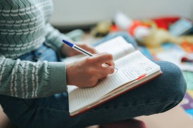 Bir insan yere bağdaş kurup bir günlüğe kalemle notlar yazar. Yumuşak atmosfer, etrafa saçılmış renkli oyuncaklar ve dekorlarla güçlendirilir..