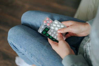 Bacak bacak üstüne atmış, elinde çeşitli ilaç paketleri olan bir adam kanepeye oturur. Ortam sakin ve özel, bu da bir anlık kişisel sağlık hizmetine işaret ediyor..