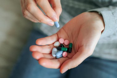 Bir insan rahat bir şekilde otururken elinde farklı ilaç ve kapsüllerden oluşan bir karışım tutar..