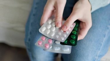 Tanınmayan bir kadın, hafif battaniyeyle kaplı bir şekilde kanepeye oturuyor ve elinde farklı türde yakın çekim tabletleri tutuyor. Evde ambulans için gereken her şeyin olması iyidir..