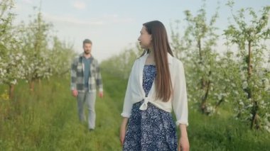 Genç bir çift, yemyeşil ve bahar çiçekleriyle çevrili çiçek bahçesinde güneşli bir yürüyüş yapar. Kaygısız ve romantik bir açık hava anını yakalar..