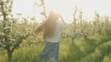 Bereketli tarlalarda ve çiçek açan ağaçlarda yürüyen, canlı, özgür ve bahar güneşinde gençlik enerjisiyle dolu mutlu bir kadının arka görüntüsü..