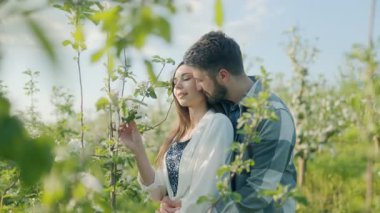 Taze çiçekler ve yeşil yapraklarla çevrili, bahar güneşi altında sevgi dolu bir çift, şefkat ve sükunetle dolu romantik bir anın tadını çıkarıyor..