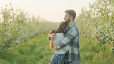 Çiçek açan ağaçların arasında yakalanan genç bir çift, sakin, samimi bir kucaklaşmayı paylaşıyor, dinginliği, güzelliği ve birlikte aydınlık bir bahar gününün vaadini kutluyor..