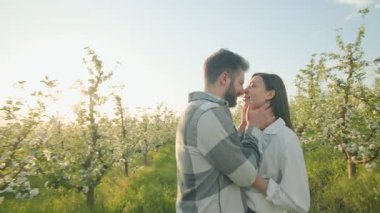 Çiçek açan dallar ve taze yeşil yapraklar arasında, iki aşık sıkıca sarılıp, açık havada romantizm, mutluluk ve ilkbahar barışı için mükemmel bir an yaratıyor..