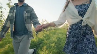 Bir kadın ve bir adam çiçek açan ağaçlarla dolu yemyeşil bir meyve bahçesinde el ele dolaşıyorlar. Günbatımının ılık ışığı birlikte neşeli bir anı paylaşırken romantik bir atmosfer yaratır..