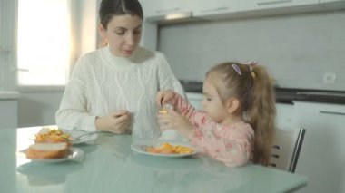 Mutfak masasında birlikte yemek yiyen bir anne ve kızının neşeli bir sahnesi, sıcaklığı, ilgiyi ve ebeveynler ve çocuklar arasındaki bağı gösteriyor..