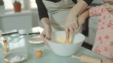 Yakın planda çekilmiş dokunaklı bir aile sahnesi: bir anne ve kızı birlikte bisküvi için hamur hazırlıyor, pişirme yoluyla bağlarını güçlendiriyor..