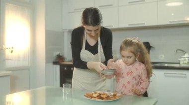 Bir anne ve küçük kızı taze pişmiş bisküvilerin üzerine şeker serperken mutfakta birbirlerine bağlanıyorlar. Evde sıcak ve yaratıcı bir aile aktivitesi..