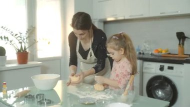 Bisküviler için hamur karıştıran bir anne ve kız, malzemeleri ve sıcaklıkla çevrili aydınlık evlerinin mutfağında sevgi dolu bir aile anını paylaşıyorlar..