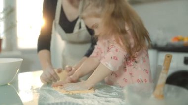 Pişirme aletleri ve malzemeleriyle çevrili bir anne ve kız bisküvi hamurunu karıştırıyor, ev mutfaklarında sıcak ve neşeli bir aile geleneğinin tadını çıkarıyorlar..