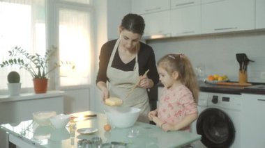 Bir anne ve küçük kızı evde kaynaşırken tencerede bisküvi pişiriyorlar, sıcak mutfakta eğlenceli bir aile aktivitesinin tadını çıkarıyorlar..