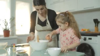Bir ev mutfağında bisküvi hamuru hazırlamak için birlikte çalışan bir anne ve kızın nefis bir sahnesi, tencereye yumurta kırmak...