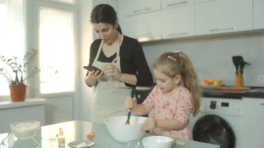 Mutfakta ebeveyn-çocuk aktivitesi, bisküvi hamurunu bir tencereye karıştırmak, evde sevgi ve takım çalışmasını sembolize ediyor..