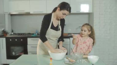 Bir anne ve kız kurabiye için hamur hazırlarken gülüp şakalaşıyorlar. Mutfakta sevgi ve kahkahalarla dolu neşeli bir aile bağı ve eğlence anı.