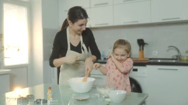 Pişirme bir komedi şovu haline gelir. Bir anne ve kız kahkaha atar, şaka yapar ve kurabiye hamuru hazırlar. Mutfakları bir neşe ve bağlantı sahnesine dönüşüyor..