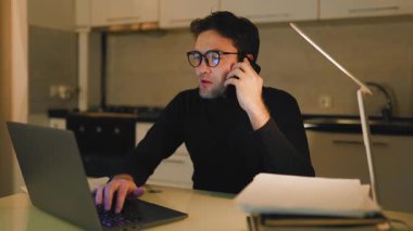 Bir adam gece geç saatlere kadar mutfakta çalışıyor. Kulağına bir telefon tutarak bilgisayarında daktilo yazıyor. Ilık ışık altında görevlerine odaklanıyor..