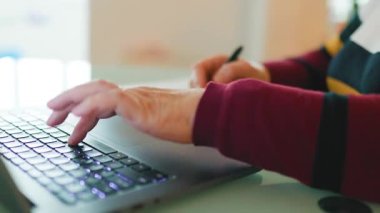 Bir insan sabahları evde dizüstü bilgisayar kullanarak ders çalışıyor ve kalemle not alıyor. Çalışma alanı sakin ve düzenli, odaklanmayı ve üretkenliği teşvik ediyor..