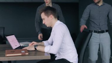 Üç profesyonel şık bir ofis masasında bir tartışmaya giriyorlar. Dizüstü bilgisayar grafikleri gösterirken bir adam diğeriyle tokalaşıyor..