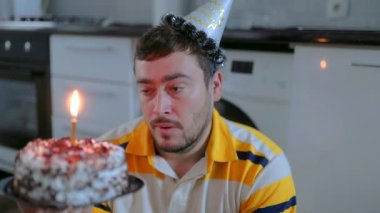 Üzgün, sakallı beyaz bir adam evde tek başına oturup doğum günü pastasının üzerine mum üflüyor. Yalnız kutlama, yalnızlık ve sessizlik hissini yakalar..