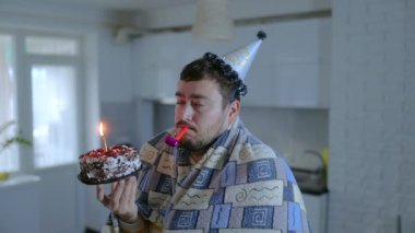 Hayal kırıklığına uğramış bir doğum günü kutlaması, battaniyeye sarılı yalnız bir adam, elinde bir pasta tutarak ıslık çalıyor, evde yalnızlığı ve üzüntüyü yansıtıyor..