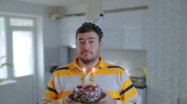 Evde 42. doğum gününü tek başına kutlayan ciddi bir adamın portresi. Yansıtıcı ve neşeli bir anda elinde mumlarla elinde bir pasta tutuyor..