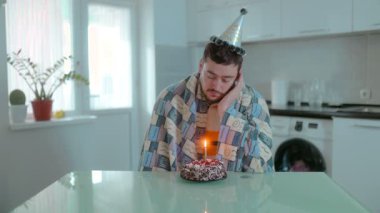 Üzgün, sakallı bir adam mutfak masasında sessizce oturur, mum ışığında doğum günü pastasına bakar, kendini yalnız ve hayal kırıklığına uğramış hisseder..