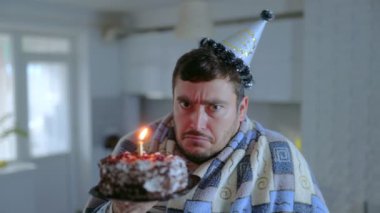 Yalnız bir doğum günü kutlaması parti şapkası ve battaniyesi içinde elinde yanan bir pasta tutan bir adamı resmediyor, görünen o ki üzgün ve sessiz bir evde yalnızlığını yansıtıyor..