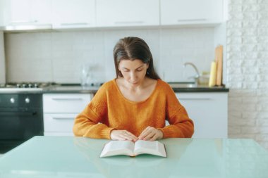 Genç dindar bir kadın mutfak masasında oturmuş İncil okumakla meşgul. Onun bağlılığı evdeki huzurlu ve düşünceli bir anı yansıtıyor..