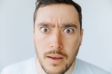 Bir adam şaşkınlık ve merak göstererek, geniş gözleri ve hafif açık bir ağızla dikkatle bakar. Arka plan parlak ve nötr. Yüz ifadesini açıkça vurguluyor..