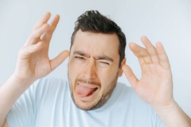 Açık mavi gömlekli bir adam aptal bir yüz ifadesi takınıyor, dilini uzatıyor ve tiksindirici bir şekilde ellerini kaldırıyor. Bu sahne, kapalı alanda neşeli bir anı yakalar..