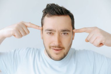 Kendi düşünceleriyle meşgul olan bir adam, tapınağına odaklanmış bir ifadeyle işaret eder. Arka planda yumuşak bir ışık var. Dalgın atmosferi arttırıyor..