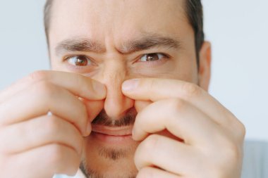 Bir adam iki eliyle burnunu sıkarken rahatsız olur. Parlak kapalı mekan ışığı, onun yüz hatlarını ön plana çıkarıyor, açık bir rahatsızlık hissi veriyor..