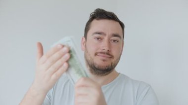 Bir adam elinde bir tomar para tutarken kendine güvenen bir gülümseme sergiliyor. Ayarlar tarafsız, odaklanmış tavrını ve elindeki para birimini vurguluyor..