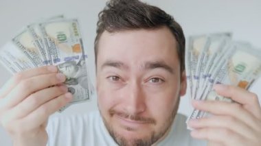 Neşeli bir yüzü olan bir adam her iki elinde de tomar tomar para gösterir. Ayar iyi aydınlatılmış, gündüz izlenimi veriyor ve mutluluk ve mali başarı hissi veriyor..