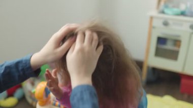 Genç bir çocuk saçlarını bir yetişkin tarafından şekillendirilirken parlak bir şekilde gülümser. Renkli oyuncaklar ve rahat bir oda bu neşeli anda neşeli bir atmosfer yaratır..