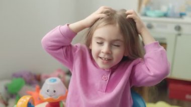 Uzun saçlı neşeli bir kız oyuncaklarla dolu renkli odasında neşeyle oynuyor. Çevresiyle etkileşim kurarken ve heyecan gösterirken parlak bir şekilde gülümsüyor..