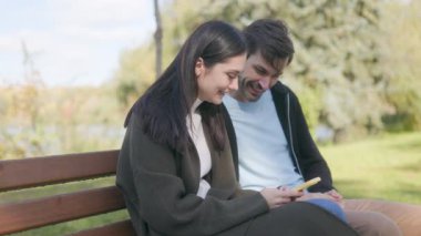 Huzurlu bir sonbahar parkında, bir çift akıllı telefona bakarken sırıtarak neşe dolu bir anı paylaşır. Aralarındaki bağ mevsimlerin güzelliği ile gelişir..