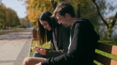 Akıllı bir telefonla nişanlanmışlar. Birkaçı parktaki bankta gülüp yakınlaşmışlar. Huzurlu sonbahar sahnesi onların duygusal bağlantılarını güçlendiriyor ve mutluluklarını paylaşıyor..